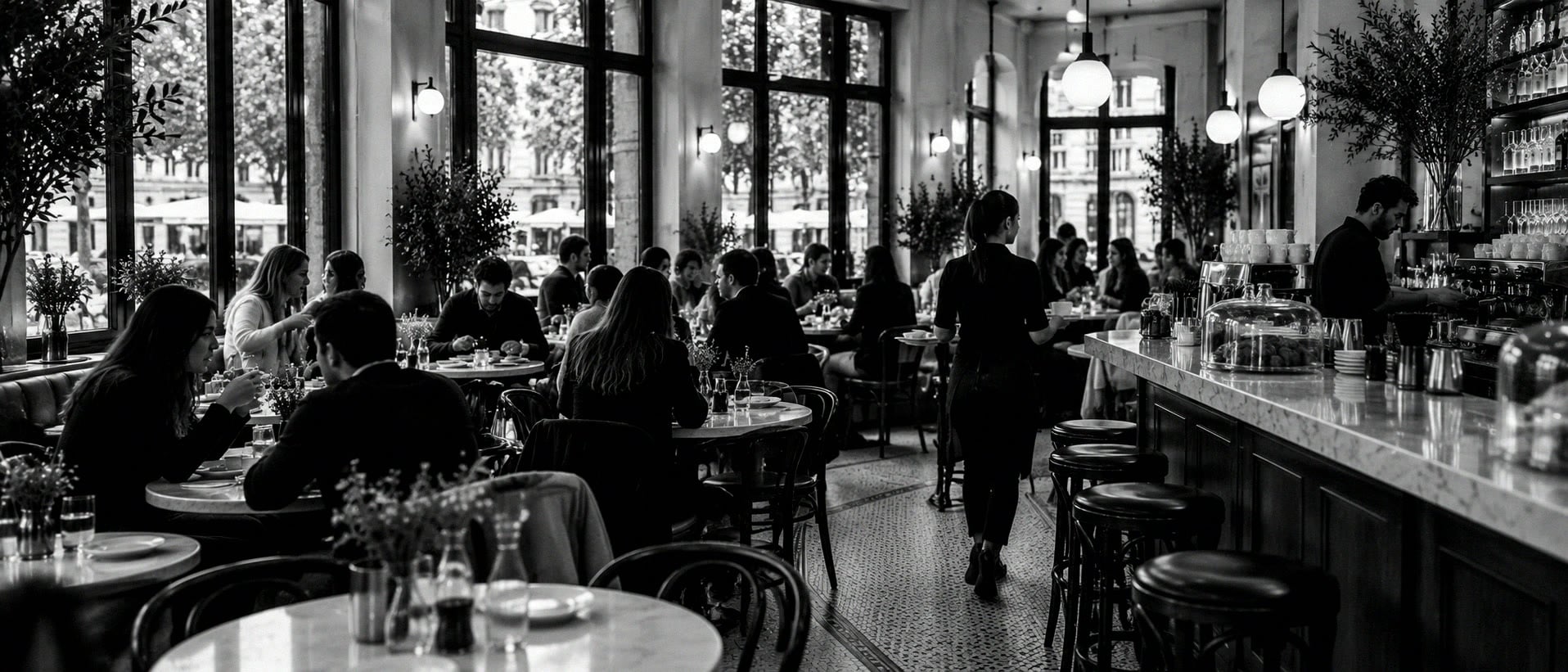 A busy neighbourhood café at brunch, small marble tables full and a long counter with the espresso machine.